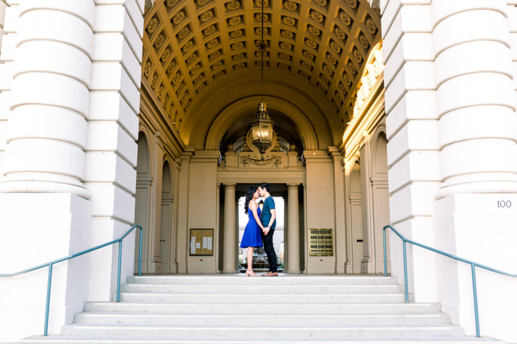 An engaged couple standing in front of the doors of the Pasadena City Hall.
