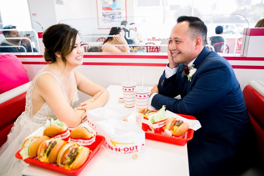 A married couple smiling at each other at an IN-N-Out Burger table with burgers and french fries in between them