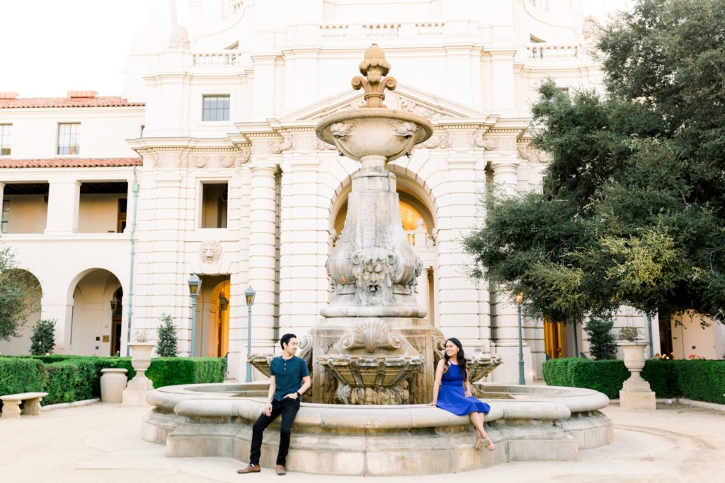 A couple sitting in front of the fountain in front of Pasadena City Hall during their engagement photo session.